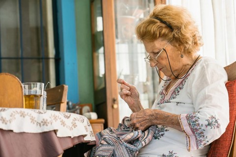 Senior woman enjoying retirement while sewing vibrant fabric, sitting comfortably beside a table