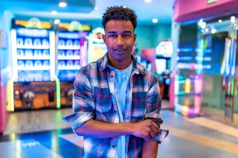 Young man standing in a vibrant arcade, surrounded by colorful lights and gaming machines, enjoying