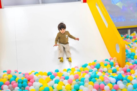 Young boy joyfully sliding into a vibrant, colorful ball pit at an indoor playground, surrounded by