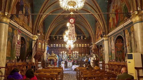 Interior of a church with paintings and chandeliers, people sitting in the pews, Easter fire
