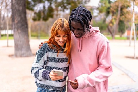 Happy multi ethnic couple sharing social media content on a smartphone while walking in a park