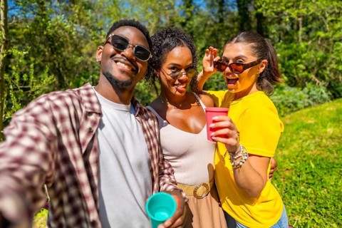 Three friends are taking a selfie while enjoying drinks outdoors, capturing a fun moment together