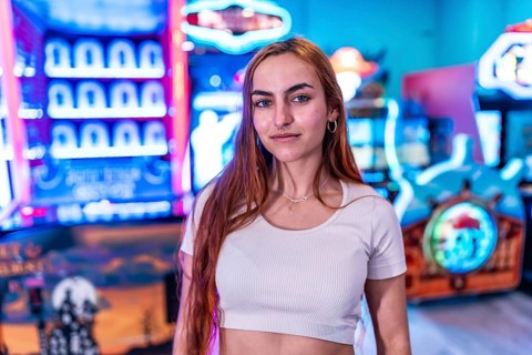 Stylish young woman standing in a vibrant amusement arcade, surrounded by colorful neon lights and