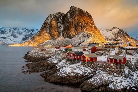 Fishermen's Village in front of snowy mountain range at the coastline in winter, Lofoten, Norway,