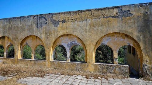 Dilapidated yellow arches in the exterior of a ruined building with visible structural damage, Lost