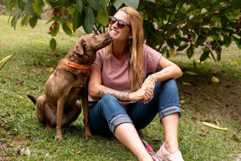 Woman in her 40s wearing sunglasses with a joyful expression receives a lick from her pet while