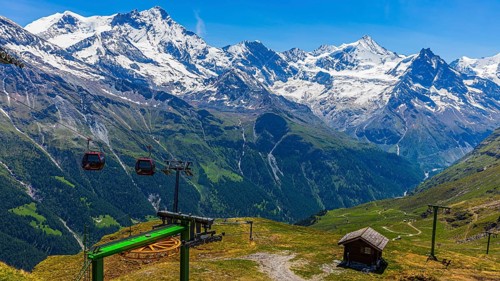 Gondolas of the cable car from Zinal to Corne de Sorebois, behind the snow-covered peaks Weisshorn,