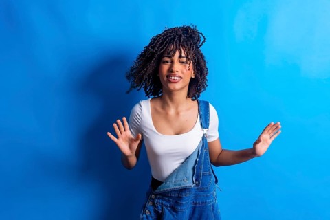 Young woman with curly hair dancing joyfully against a vibrant blue backdrop, embodying carefree