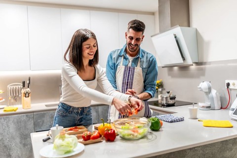 Cheerful couple smiling and preparing a healthy salad together in a modern kitchen, enjoying their