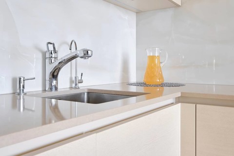 A contemporary kitchen features a polished stone countertop with a shiny faucet and a glass pitcher