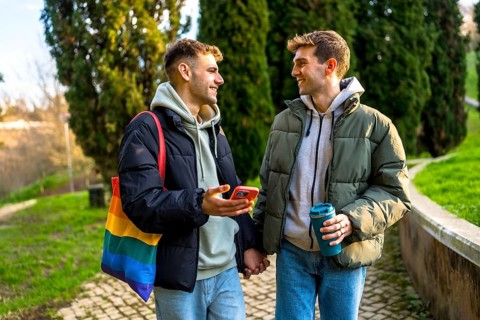 Happy gay couple holding hands and walking in a park, enjoying a relaxing day together and showing