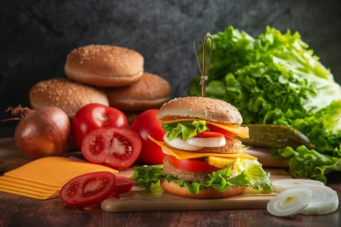 A burger with fresh vegetables on a rustic board with ingredients in the background