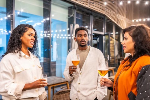 Multi-ethnic coworkers talking while drinking beer in the terrace of a night bar after work