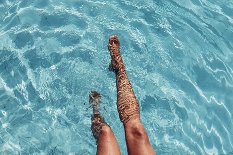 Women's legs in the water of a pool with turquoise water and summer light