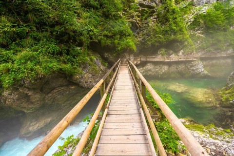 Scenic view of a wooden footbridge spanning a crystal clear emerald river flowing through the