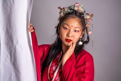 A woman in a red dress with a flower headpiece is posing for a photo. The image has a traditional