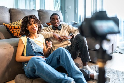 Two young content creators are recording a video blog from their living room, discussing and