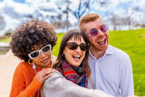 Three cheerful multi ethnic friends are taking a selfie in a park, laughing and enjoying a