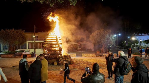 People gather around a burning pile of wood at night, some take photos, Easter fire Psinthos, Holy