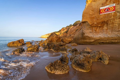 ROCKFALL UNSTABLE CLIFFS, KEEP A SAFE DISTANCE is written in English on a warning sign in Portugal