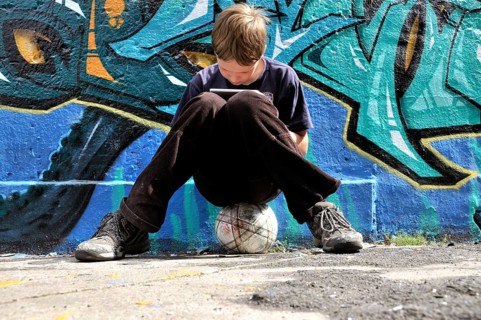 Ten-year-old boy playing with his Nintendo in front of a graffiti wall, football pitch, Germany,