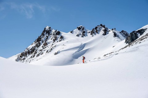 Ski tourer on the descent, minimalist winter landscape, white snow and dark mountains on the