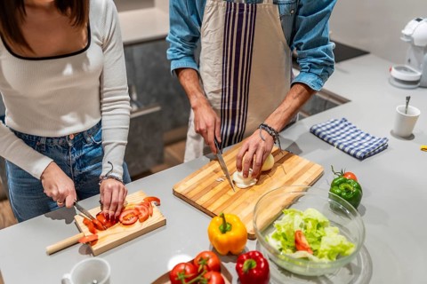 Young couple slicing fresh vegetables on wooden cutting boards, preparing a healthy salad together