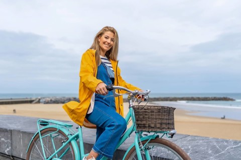 Smiling woman with yellow raincoat sitting on a light blue bicycle by the sea enjoying freedom and