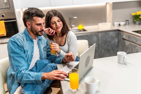Young couple sitting at kitchen table, drinking orange juice and using laptop, enjoying their time