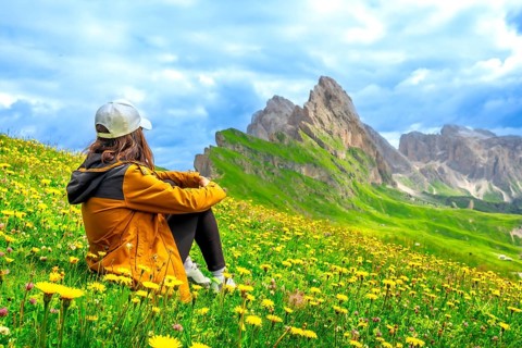 Tourist admiring seceda peaks in the italian dolomites, surrounded by yellow flowers in a sunny