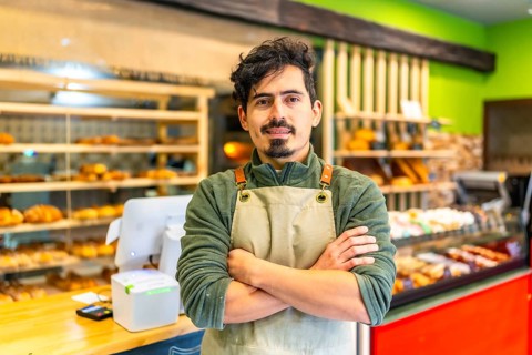Portrait of a confident latin young baker standing with arms crossed in an artisan modern shop