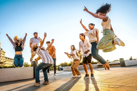 Full length photo of a group of multiracial friends jumping and dancing in the city during sunset