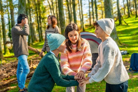 Two caucasian brothers and sister stacking hands playing in the forest enjoying camping with family