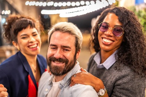 Happy diverse multi-ethnic young friends taking selfie at night party outdoors in a terrace bar