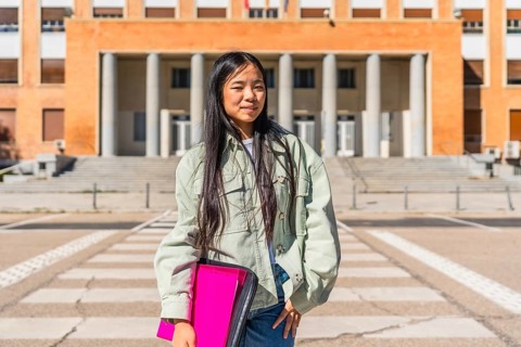Portrait of a confident chines university student standing in the street at the entrance of the