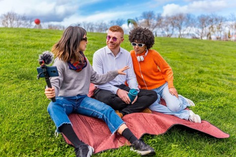Three content creators are recording an interview for their video podcast in a park, using a