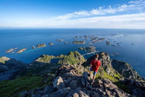 Mountaineer on the summit of Festvagstinden, view of the sea and archipelago islands with the