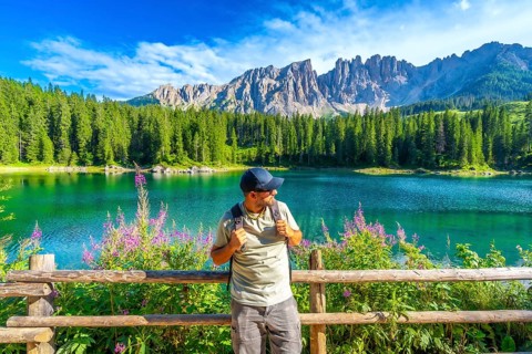 Hiker admiring the stunning scenery of lake carezza with the latemar mountain range in the