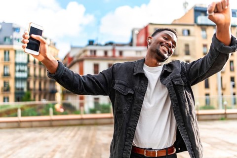 African man dancing happy while listening to music using mobile phone and wireless earbuds in the