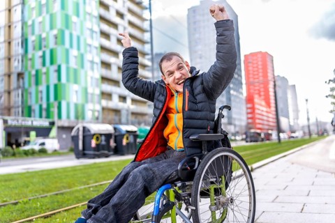 Happy disabled man celebrating in a wheelchair near modern buildings, enjoying his freedom and