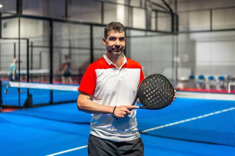 Portrait of a sportive mature man with paddle tennis racket standing in a blue indoor paddle court