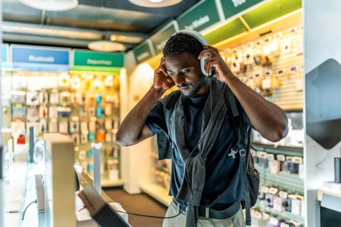 Young african man checking new headphones in electronics store standing alone