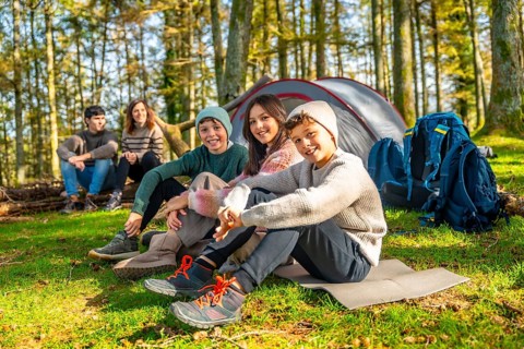 Three kids sitting next to their parents in the forest enjoying together a camping weekend