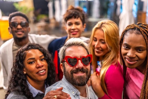 Man with heat shape sunglasses taking selfie with friends outdoors during night in the terrace of a