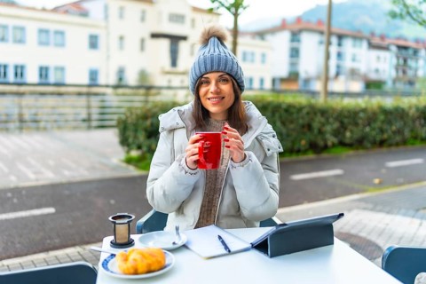 Happy beauty woman enjoying warm tea working with tablet in an outdoor sidewalk cafeteria