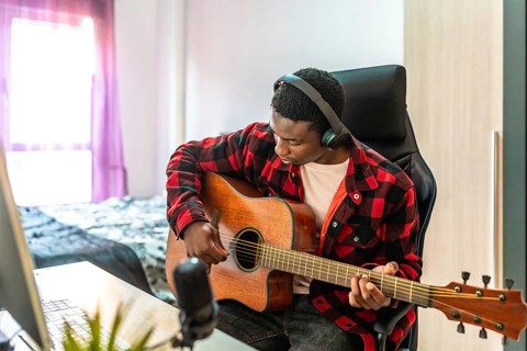 Young man playing acoustic guitar and recording music using a computer and microphone at home