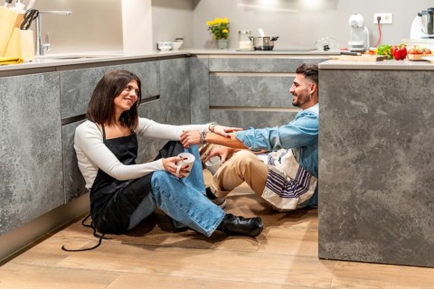 Two chefs are sitting on the floor of their modern kitchen, enjoying a coffee break and chatting