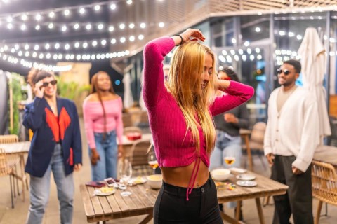 Blonde sensual woman dancing with friends at night party at the terrace of a bar decorated with