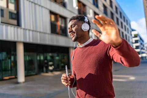 Energetic african young man listening to music and dancing while walking along a city street
