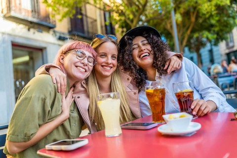 Happy female friends meeting on a bar terrace enjoying sunset at city